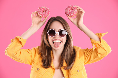 Beautiful young woman wearing sunglasses with donuts on pink background