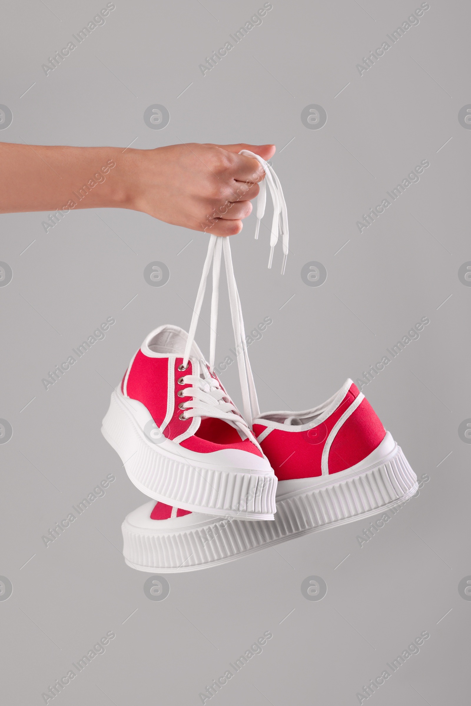 Photo of Woman holding pair of classic old school sneakers on light grey background, closeup