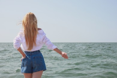 Young woman near sea on sunny day in summer, back view. Space for text