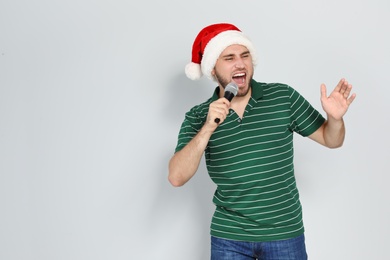 Young man in Santa hat singing into microphone on color background. Christmas music