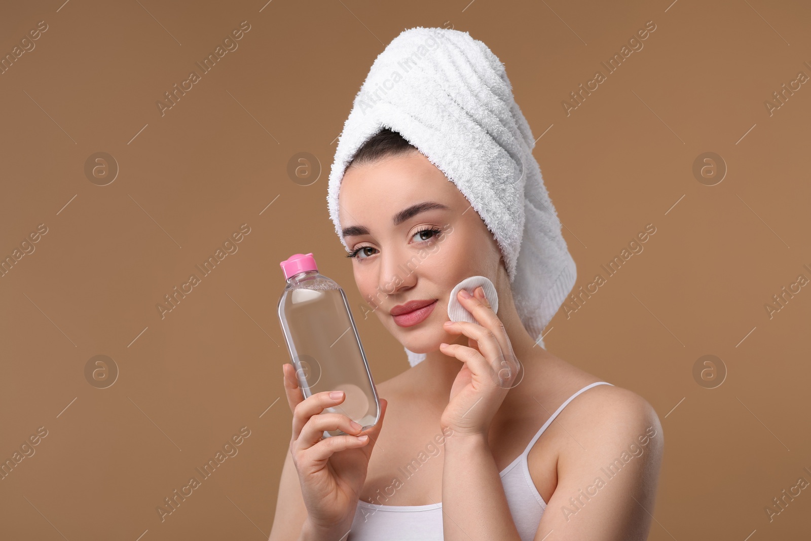 Photo of Beautiful woman in terry towel removing makeup with cotton pad on beige background