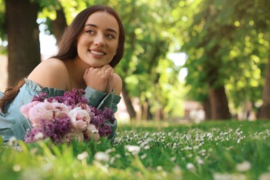 Photo of Beautiful woman with bouquet of spring flowers on green grass in park, space for text