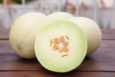 Whole and cut fresh ripe melons on wooden table outdoors, closeup