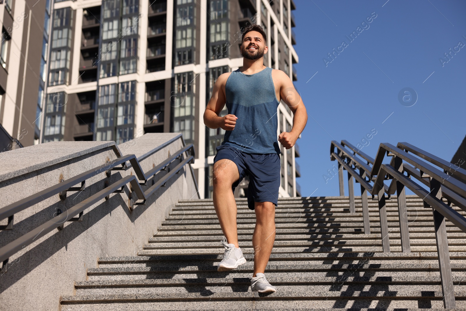 Photo of Happy man running down stairs outdoors on sunny day, low angle view