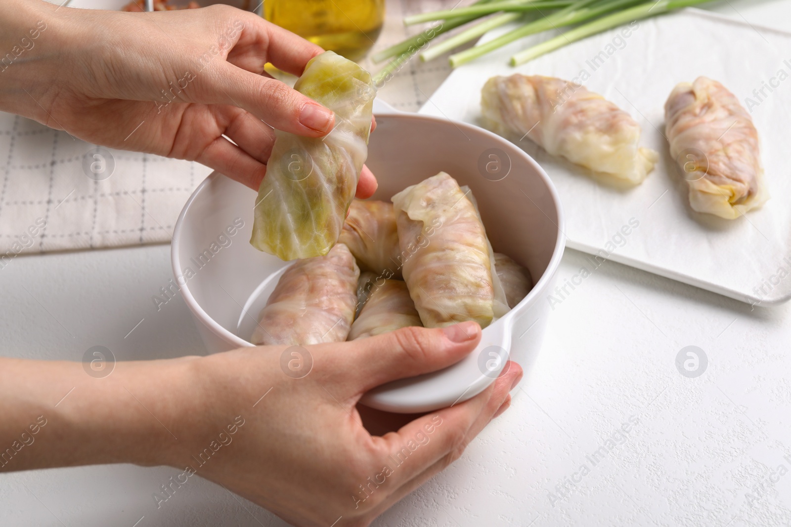 Photo of Woman putting uncooked stuffed cabbage roll into ceramic pot at white table, closeup