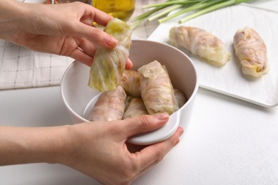 Woman putting uncooked stuffed cabbage roll into ceramic pot at white table, closeup