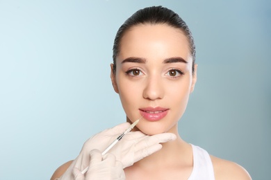 Photo of Young woman getting lip injection on color background