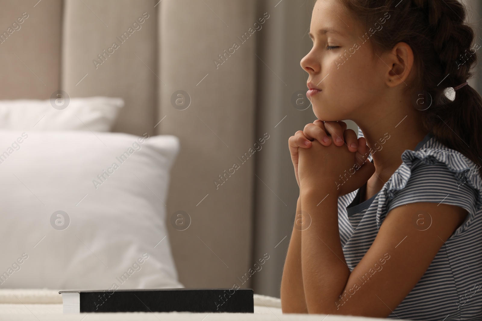 Photo of Cute little girl praying over Bible in bedroom. Space for text