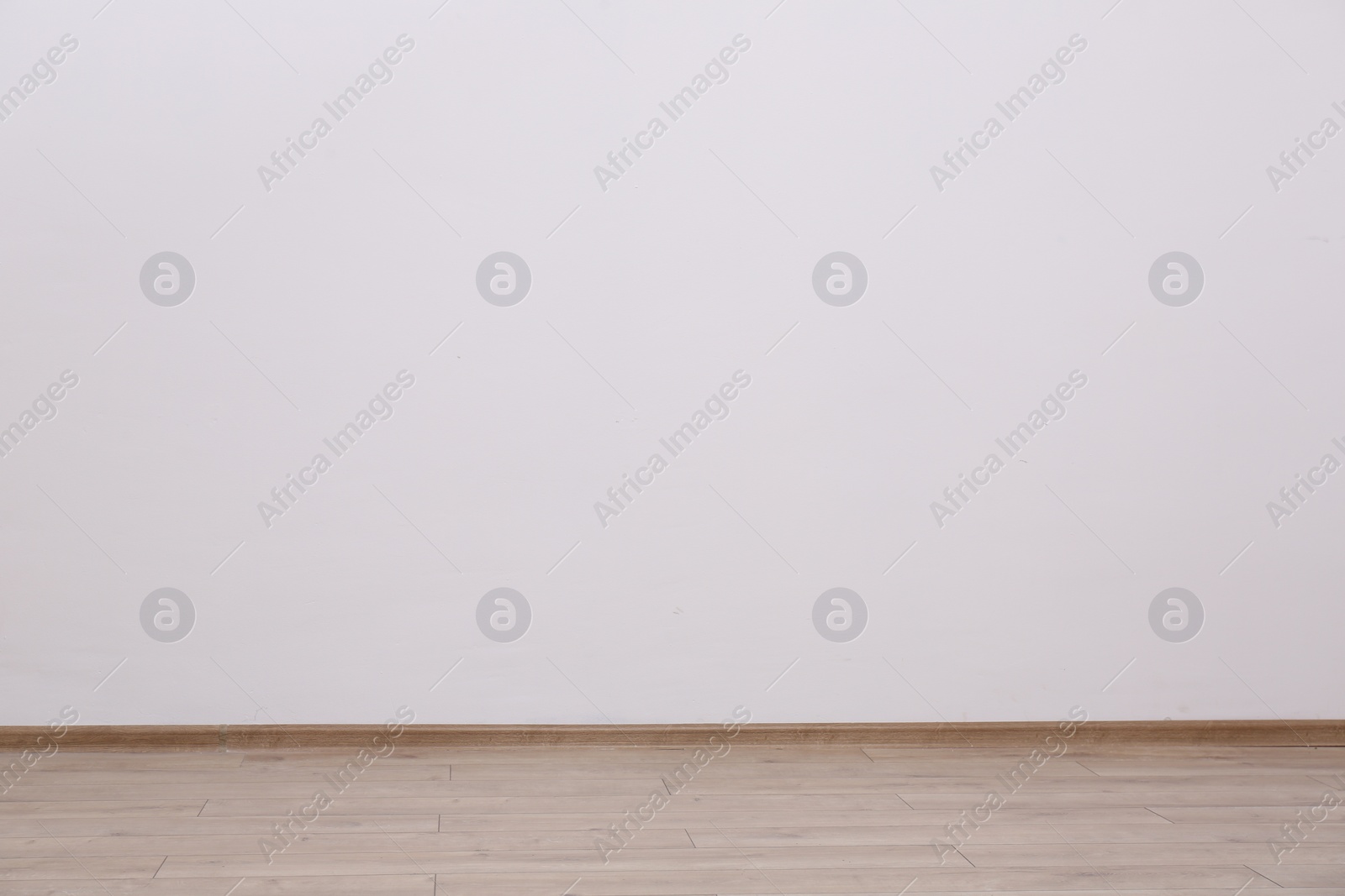 Photo of Empty white wall and wooden floor indoors, space for text