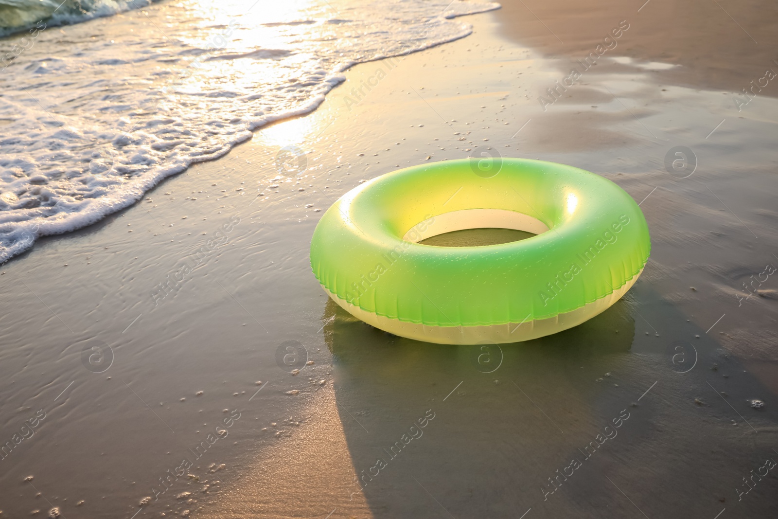 Photo of Light green inflatable ring on sunlit sandy beach near sea, space for text