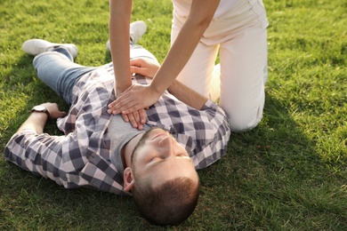 Photo of Woman doing cardiac massage to unconscious man with heart attack on green lawn