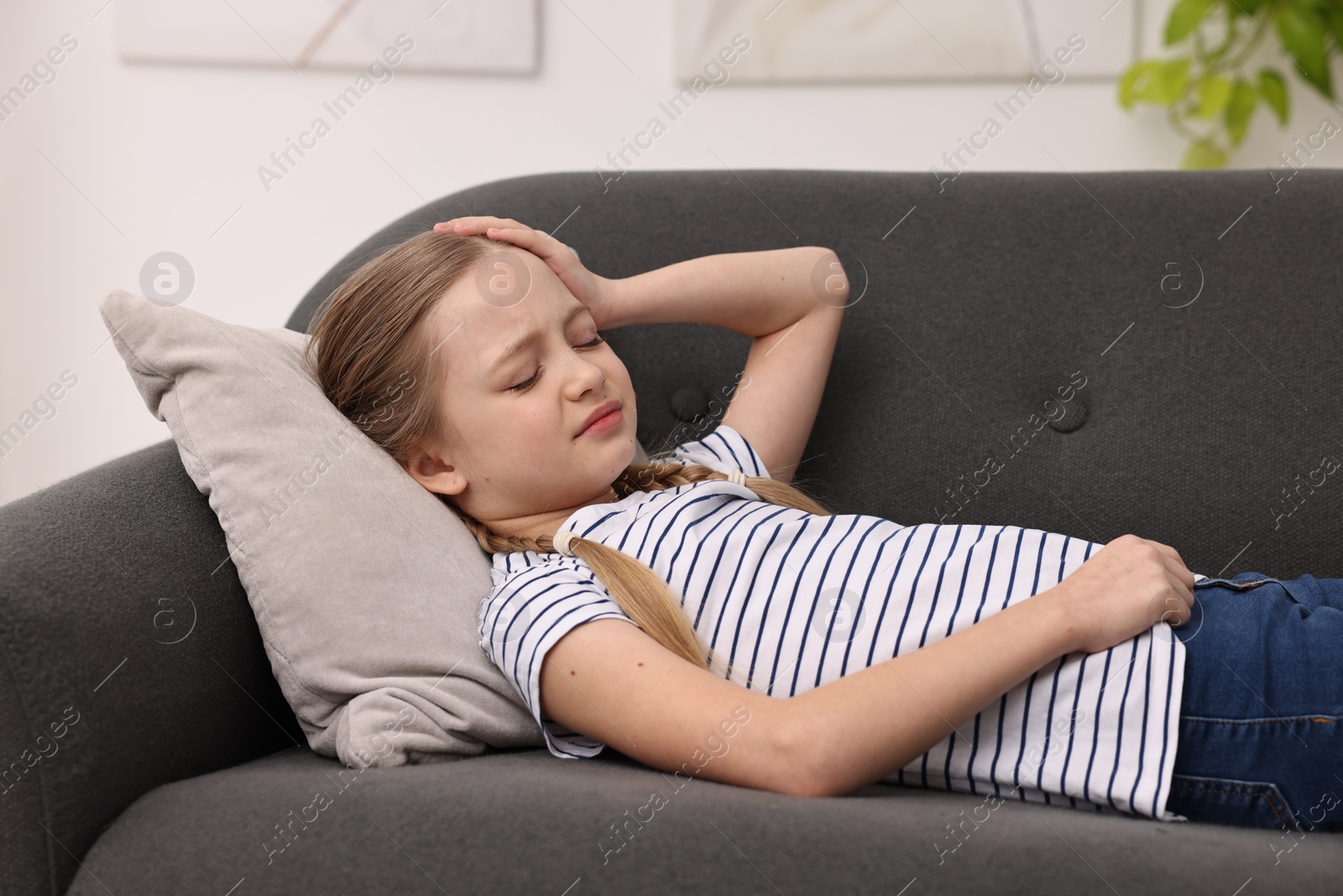 Photo of Little girl suffering from headache on sofa indoors