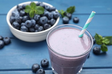 Photo of Glass of blueberry smoothie and fresh berries on blue wooden table, closeup