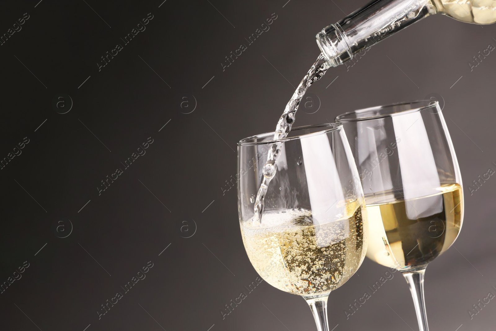 Photo of Pouring white wine into glass against grey background, closeup. Space for text