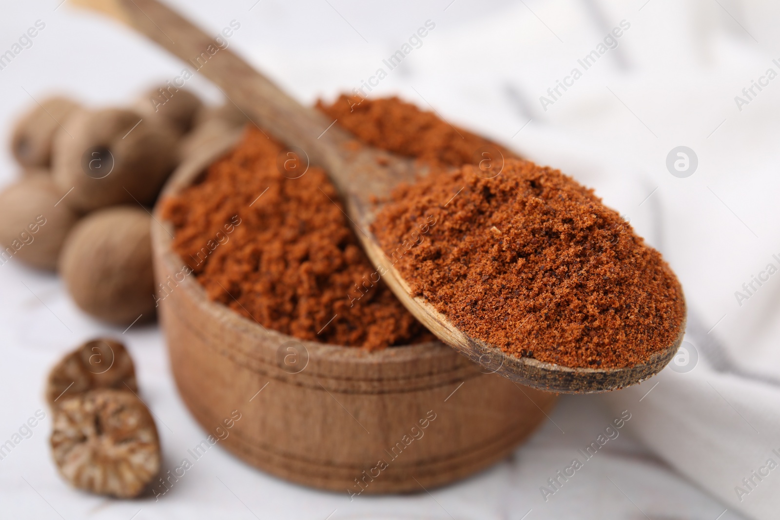 Photo of Bowl and spoon with nutmeg powder on white table, closeup