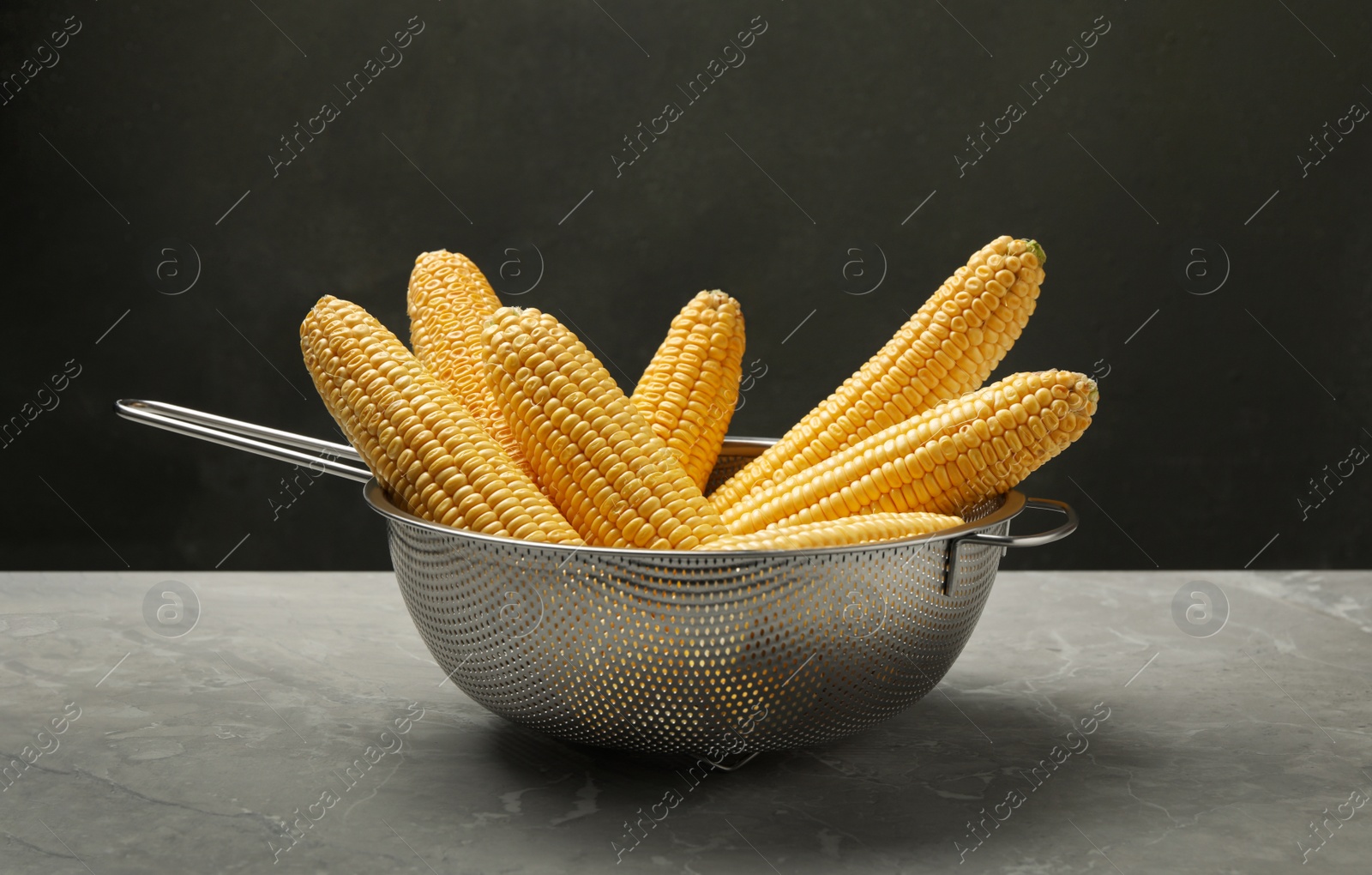 Photo of Corn cobs in colander on grey marble table