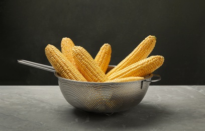 Corn cobs in colander on grey marble table