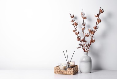 Burning candles in wicker basket and vase with cotton branches on table against white background. Space for text