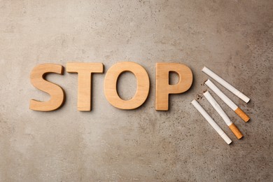 Word Stop made of wooden letters and cigarettes on grey textured table, flat lay. No smoking concept