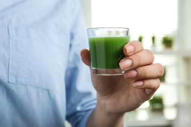 Photo of Woman holding shot glass of wheat grass juice indoors, closeup