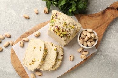 Photo of Tasty halva with pistachios and mint on light grey table, top view