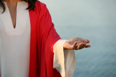 Photo of Jesus Christ reaching out his hand near water outdoors, closeup