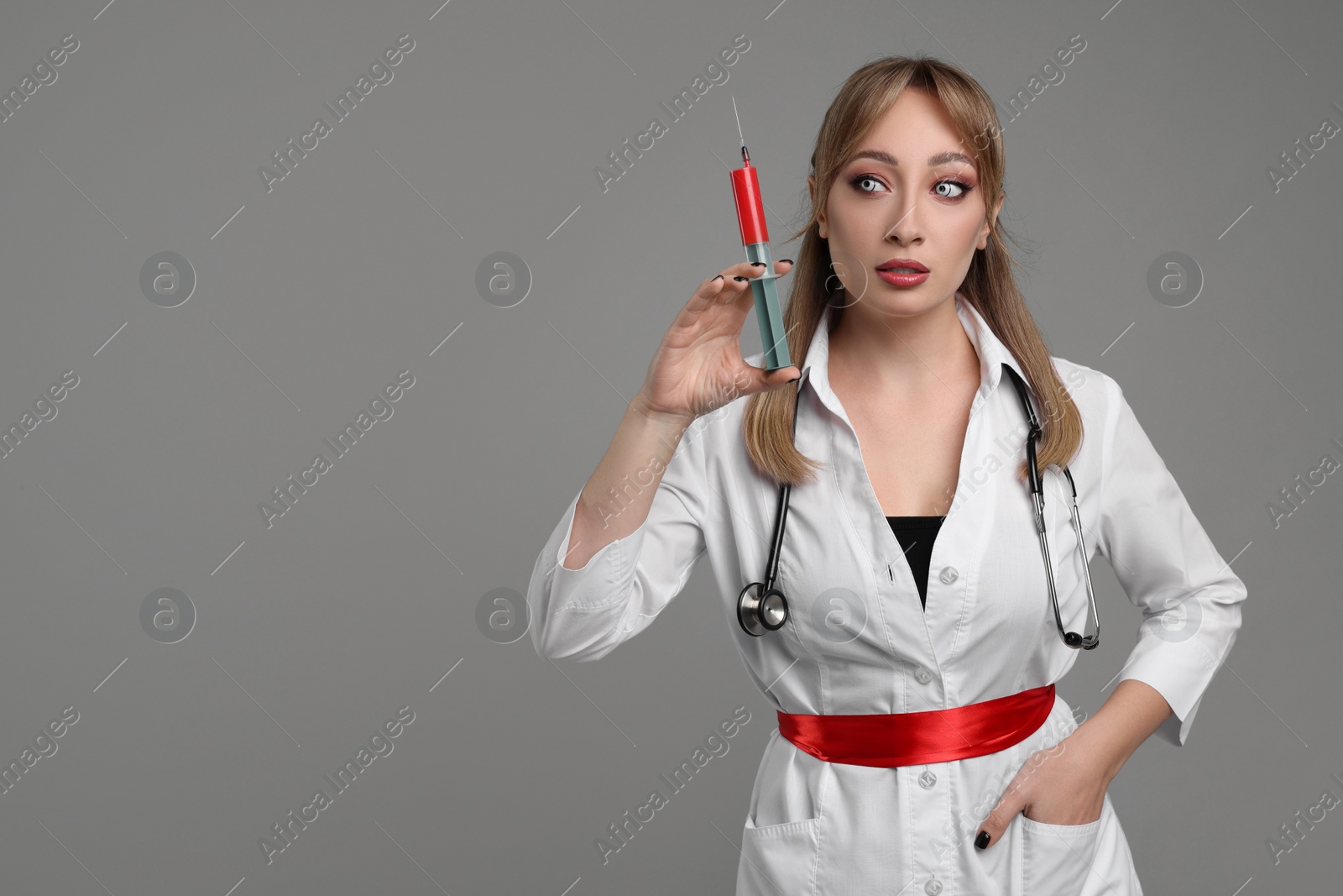 Photo of Woman in scary nurse costume with syringe on light grey background, space for text. Halloween celebration