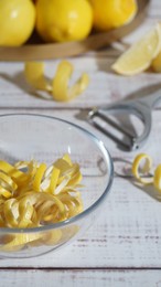 Bowl with peel pieces, fresh lemons and zester on white wooden table, closeup