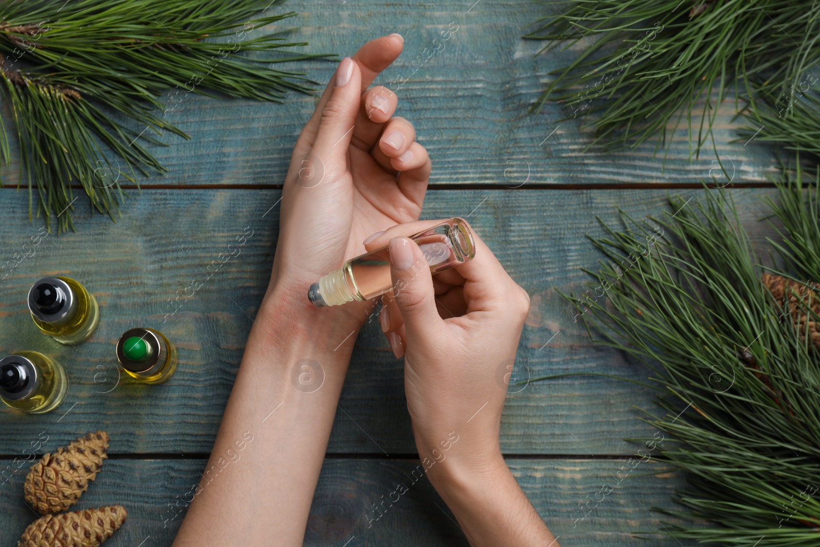 Photo of Woman applying pine essential oil on wrist at light blue wooden table, top view