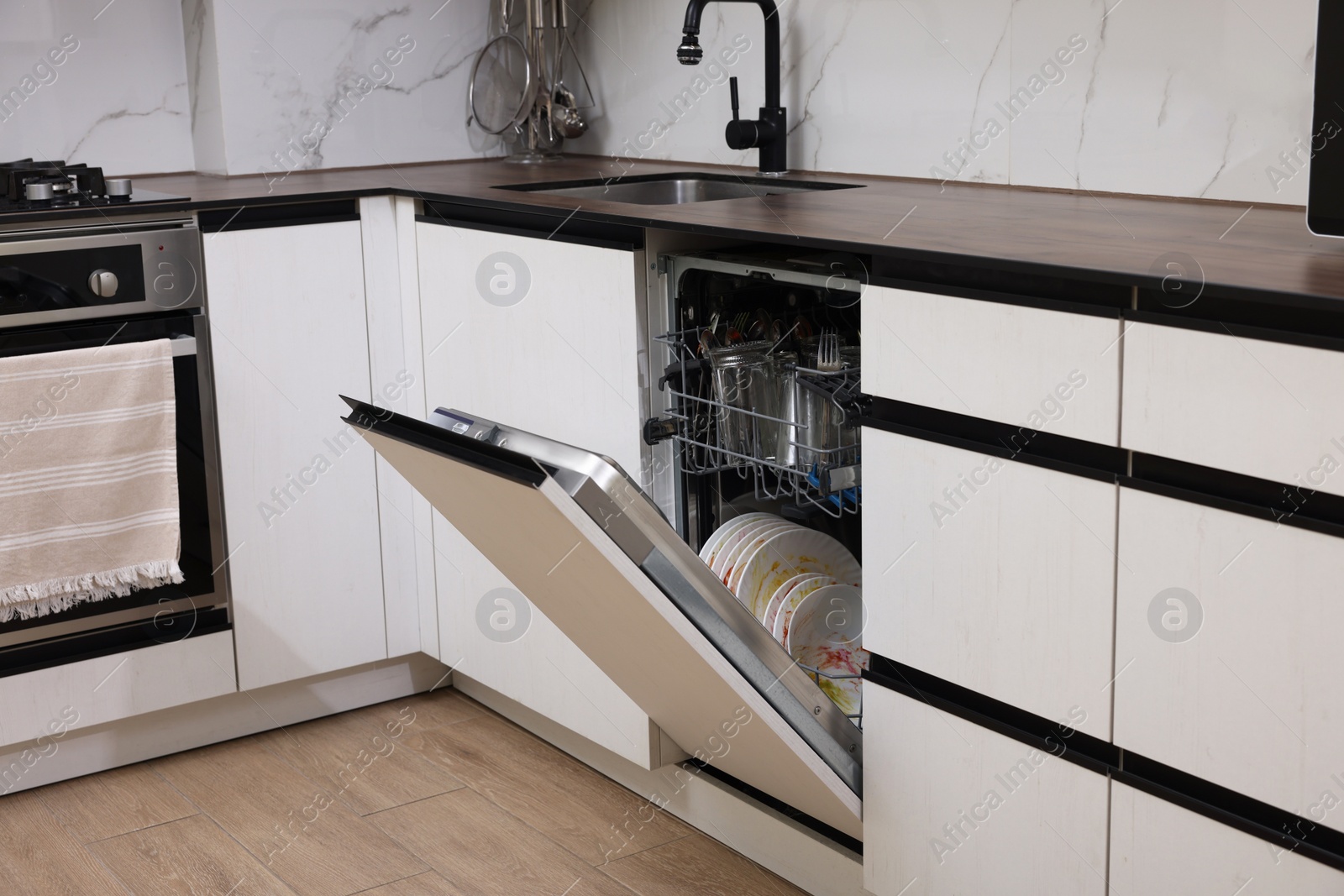 Photo of Open modern dishwasher with dirty tableware in kitchen