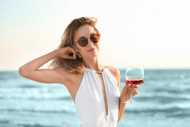 Photo of Young woman with glass of wine on beach