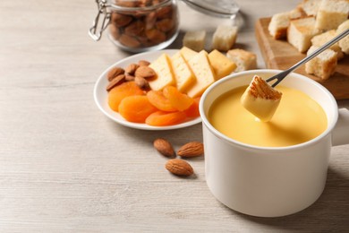 Dipping piece of bread into tasty cheese fondue on light wooden table, space for text