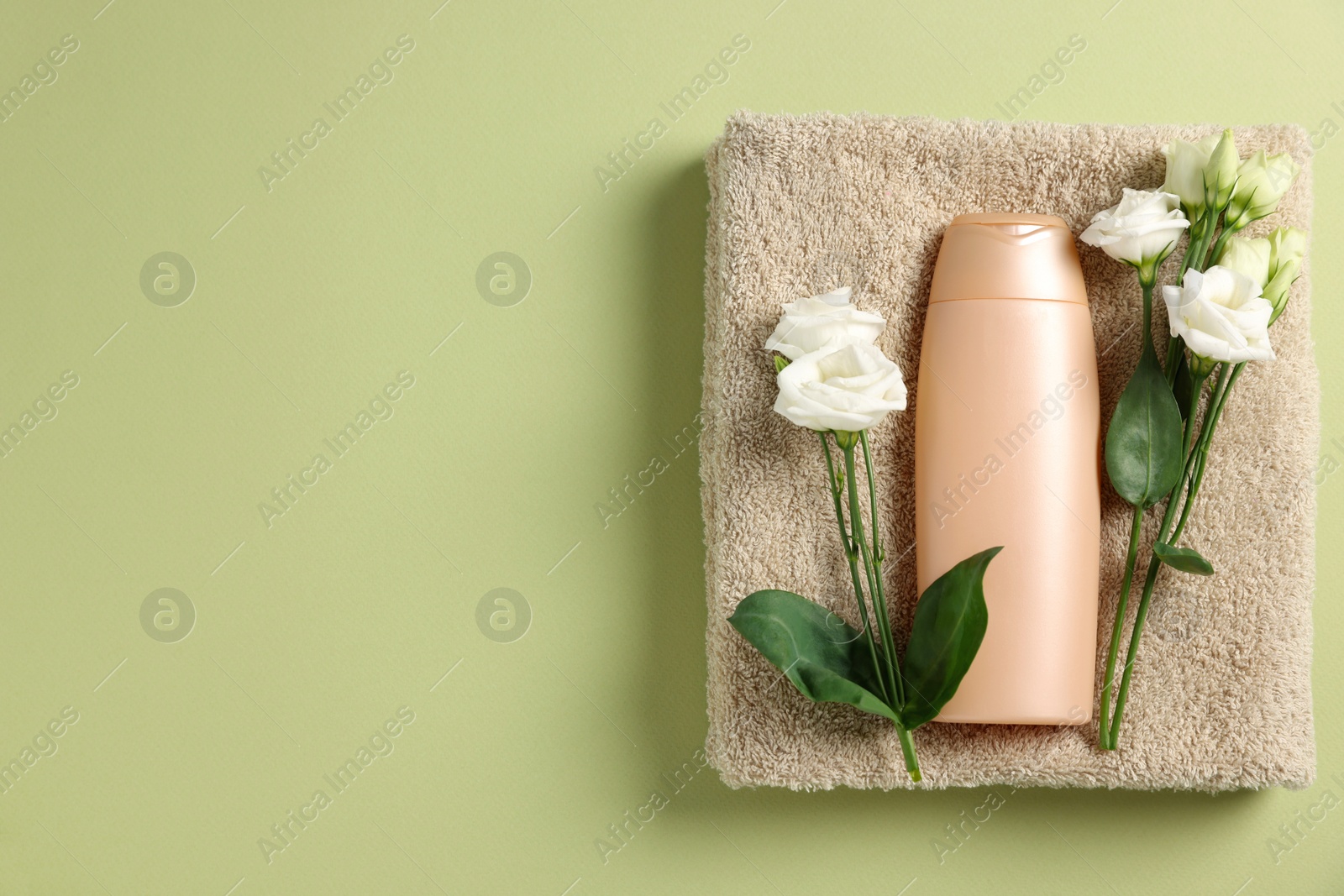 Photo of Soft folded towel with flowers and cosmetic product on green background, top view. Space for text