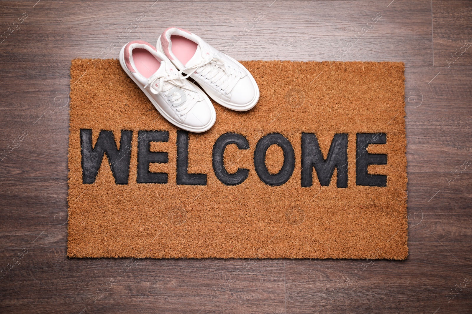 Photo of Stylish door mat with word Welcome and shoes on wooden floor, top view