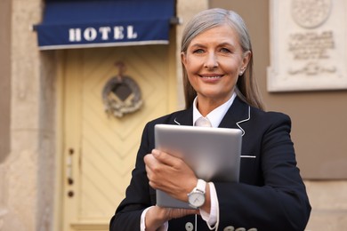 Happy business owner with tablet near her hotel outdoors, space for text