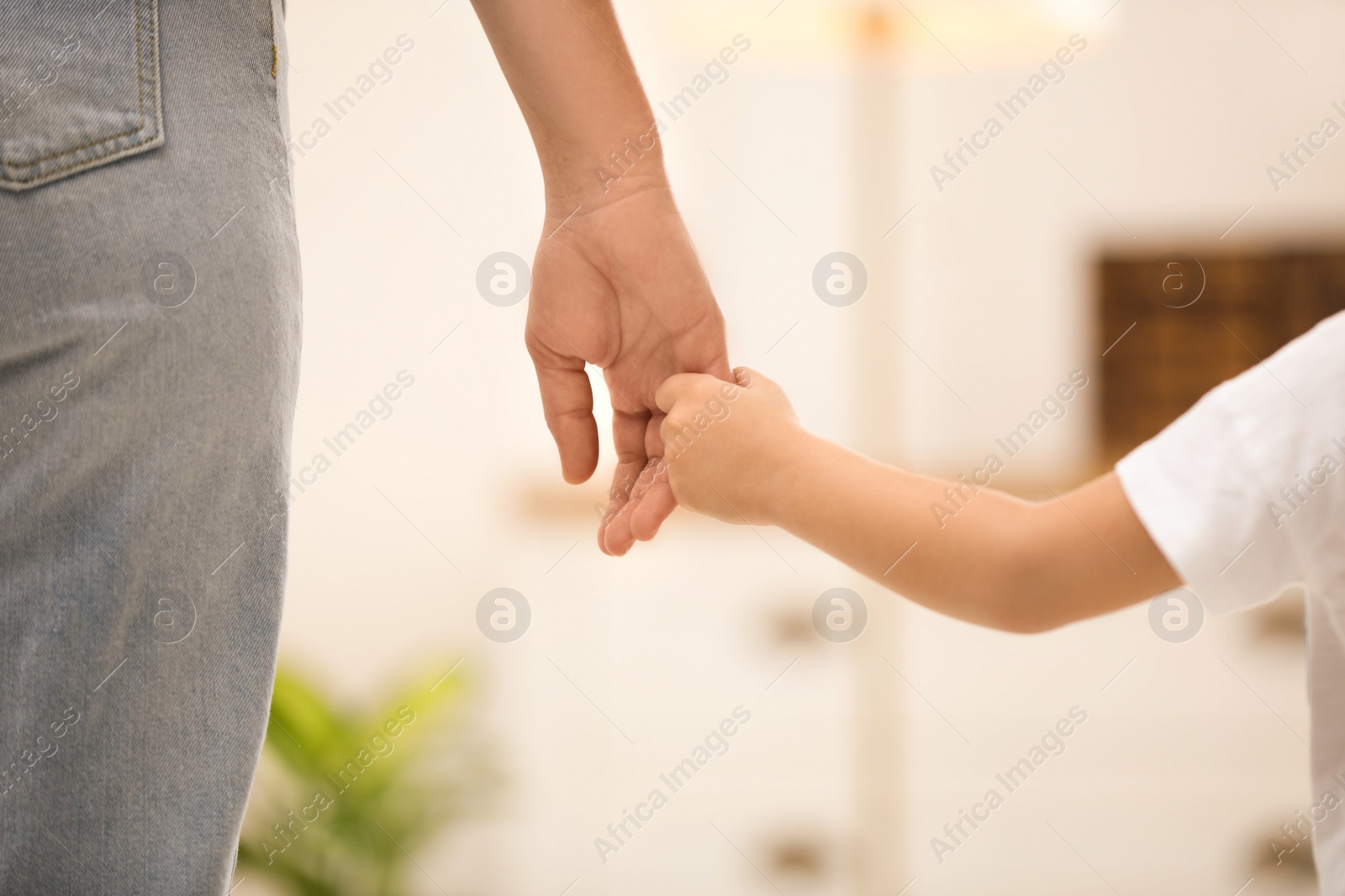 Photo of Mother holding hands with her child indoors, closeup. Happy family