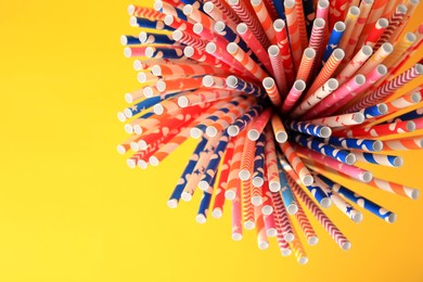 Many paper drinking straws on yellow background, top view. Space for text