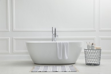 Photo of Modern ceramic bathtub and table with toiletries near white wall indoors