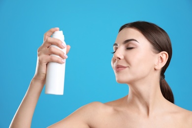 Photo of Young woman with bottle of thermal water on color background. Cosmetic product