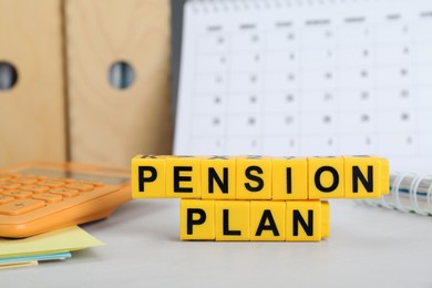 Words Pension Plan made of yellow cubes, calculator and stationery on white office table, closeup