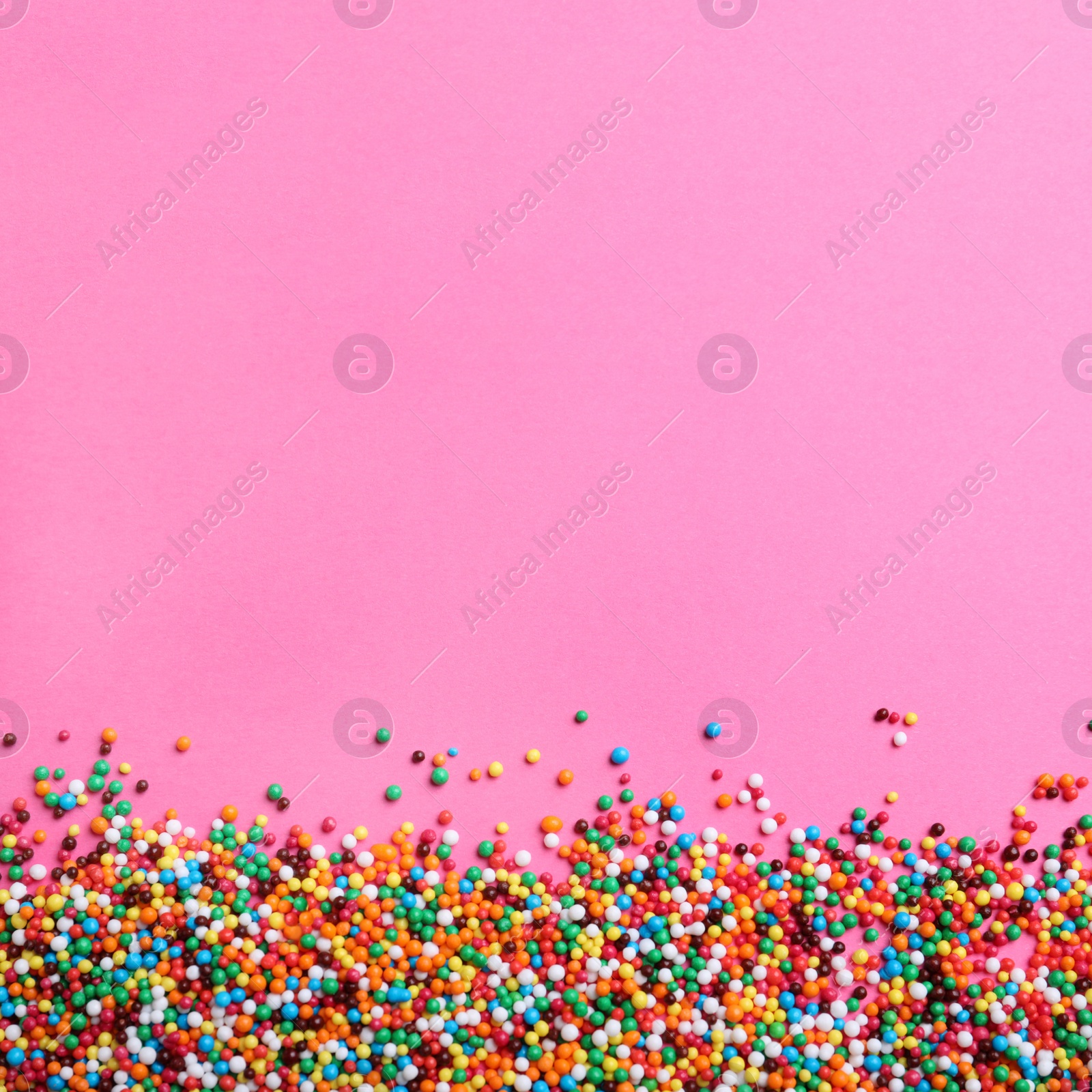 Photo of Bright colorful sprinkles on pink background, flat lay with space for text. Confectionery decor