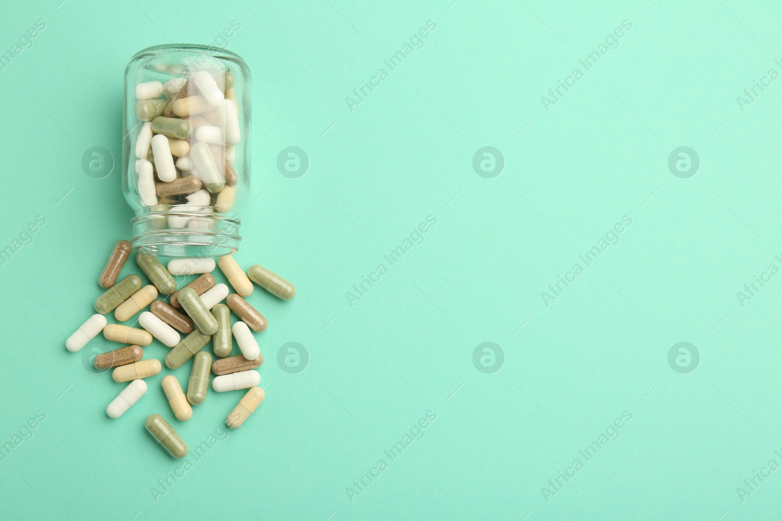 Photo of Vitamin pills and bottle on mint color background, top view. Space for text