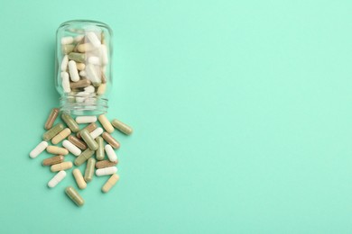 Photo of Vitamin pills and bottle on mint color background, top view. Space for text