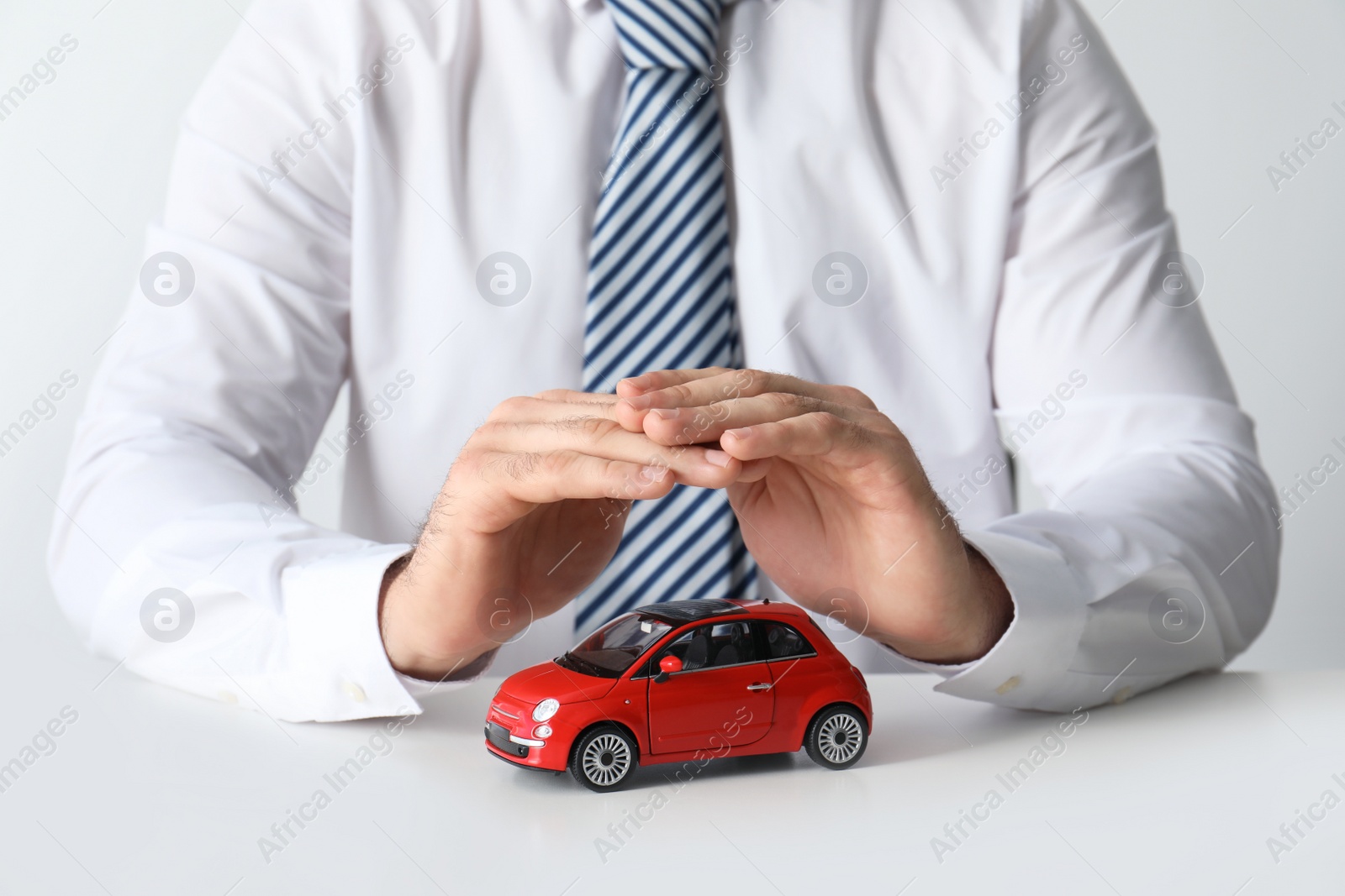 Photo of Male insurance agent covering toy car at table, closeup