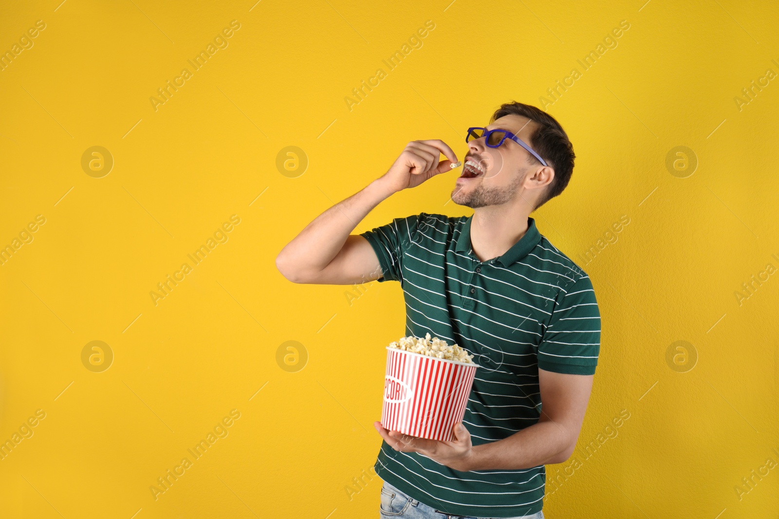 Photo of Man with 3D glasses eating tasty popcorn on color background. Space for text