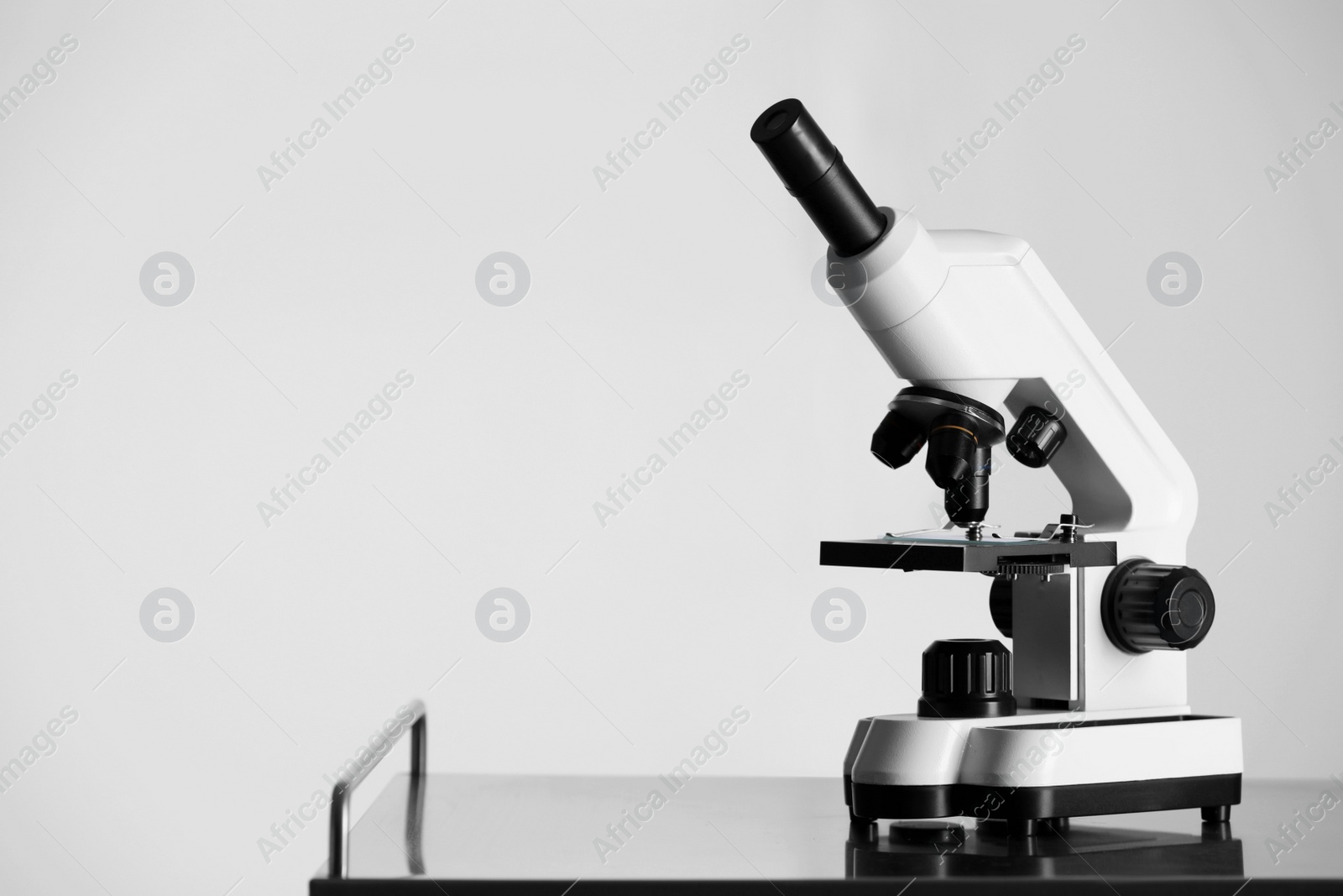 Photo of Modern microscope on metal table against light background. Space for text