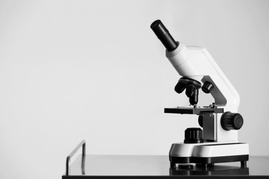 Modern microscope on metal table against light background. Space for text