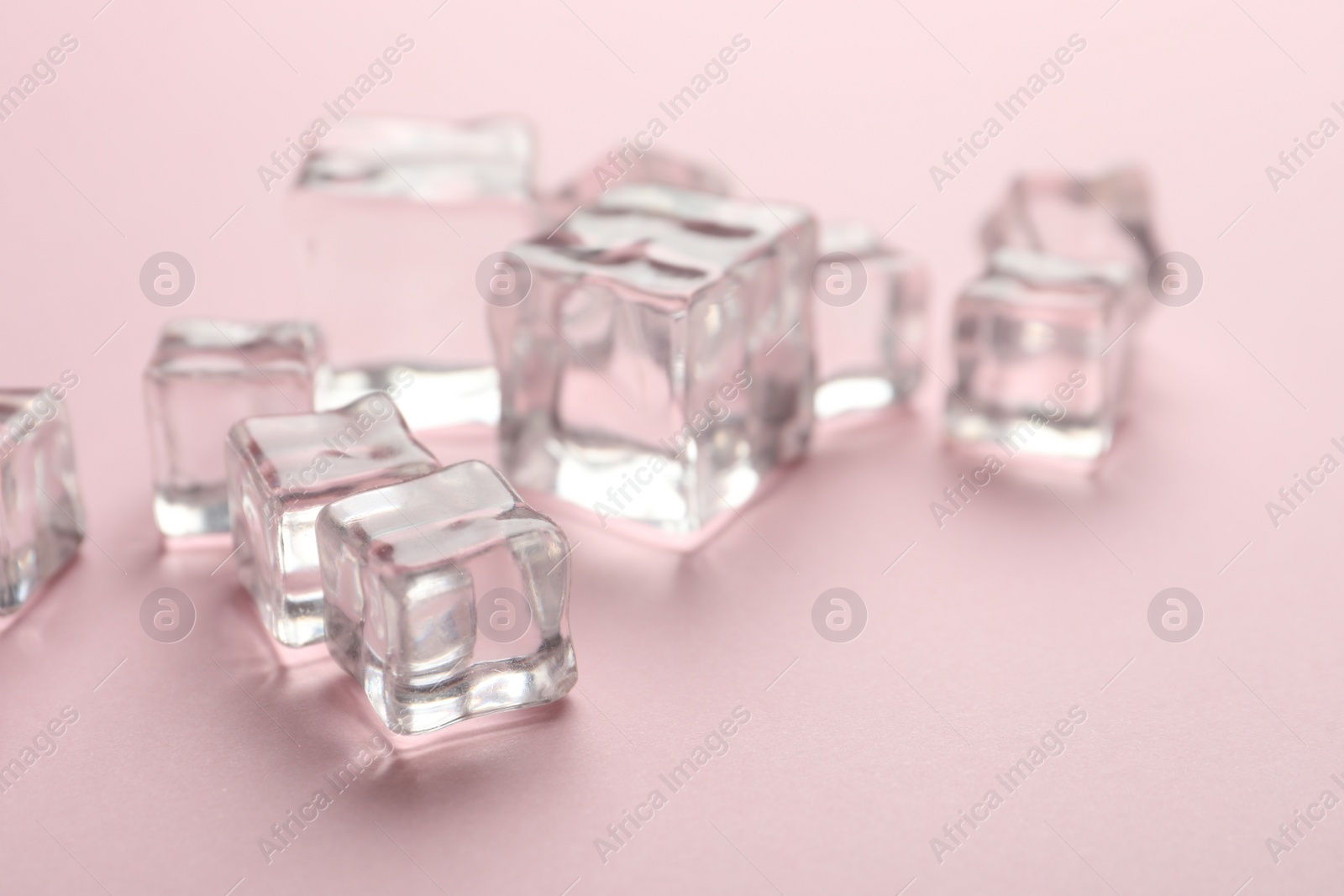 Photo of Crystal clear ice cubes on pink background, closeup