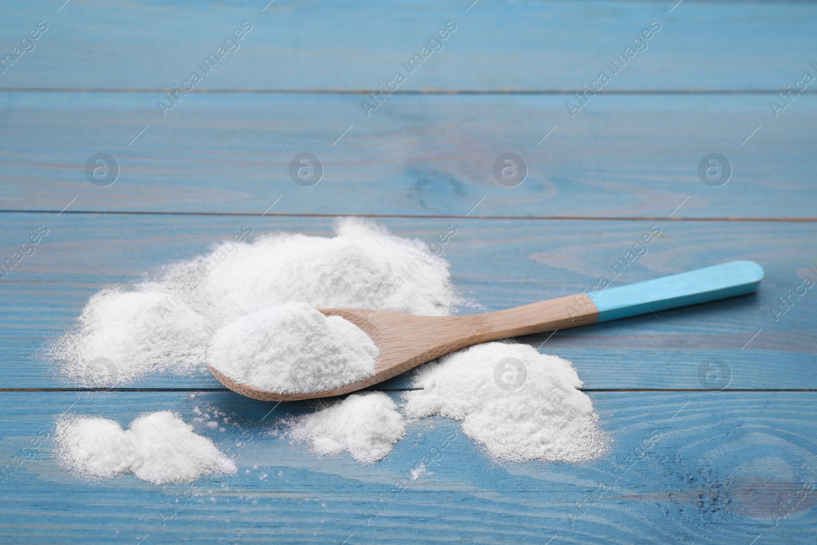 Photo of Sweet fructose powder and spoon on light blue wooden table