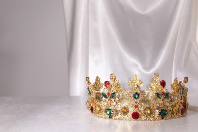 Beautiful golden crown with gems on light grey table. Space for text